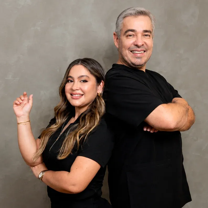 La Dra. Nayduth Alonso y el Dr. Orlando Rey, de espaldas y sonriendo, con el uniforme negro de la clínica